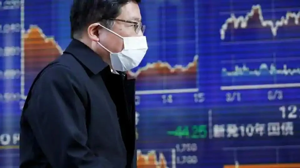 A passerby wearing a protective face mask, following an outbreak of the coronavirus, walks past an electronic board showing the graphs of the recent movements of Japan