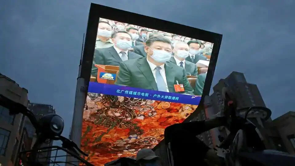 A giant screen displays news footage of Chinese President Xi Jinping wearing a face mask, following the coronavirus disease (COVID-19) outbreak, attending the opening session of the National People