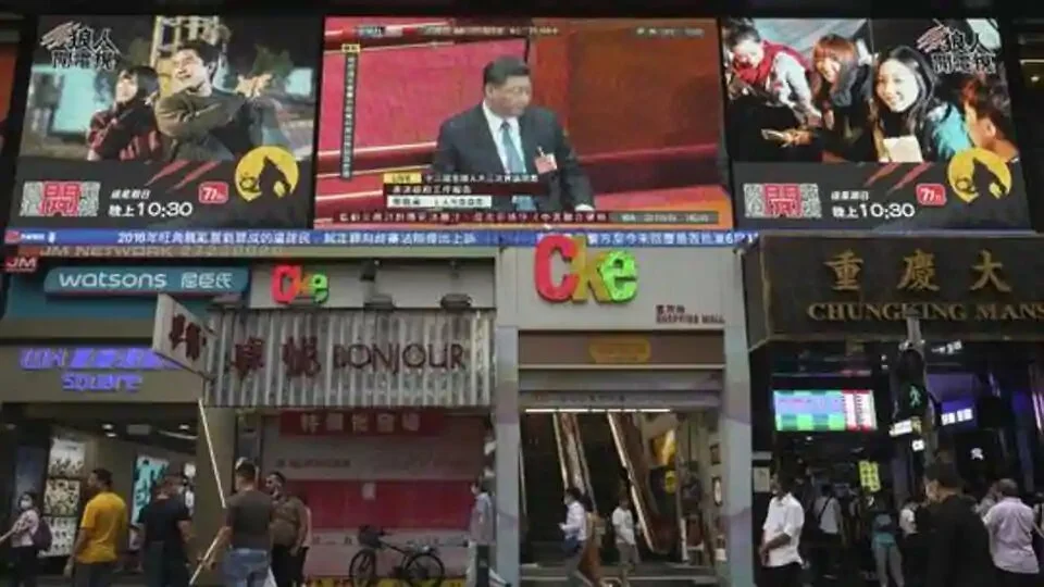 Pedestrians walk under a giant screen showing live telecast of Chinese President Xi Jinping, top center, at the closing session of the National People
