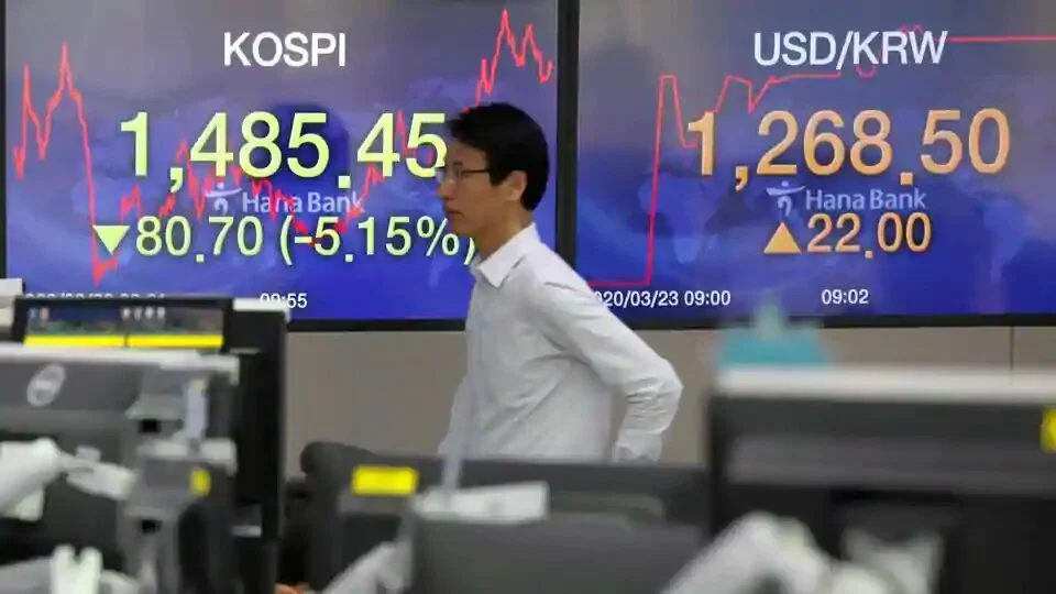 A currency dealer walks past in front of electronic boards showing the Korea Composite Stock Price Index (KOSPI) and the exchange rate between the US dollar and South Korean won, in Seoul, South Korea, March 23, 2020.